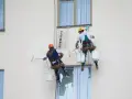Deux peintres en bâtiment travaillent en hauteur sur une façade. L'un utilise un rouleau pour la peinture immeuble, l'autre est prêt à continuer.