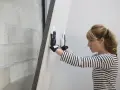 Une femme en gants manipule une plaque de doublage polystyrène expansé contre un mur de parpaings.