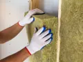 Pose d'isolant en laine de roche dans un mur. Les mains gantées ajustent le matériau pour une isolation optimale.