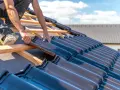 Un couvreur installe des tuiles sombres sur une toiture en bois. Un travail minutieux pour l'entretien de toiture.
