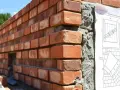 Mur en briques rouges, avec du béton de ciment visible sur le côté. Un plan de construction est épinglé.