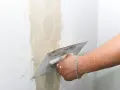 Main d'un artisan appliquant de l'enduit pour réparer une fissure crepis maison.