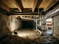 Éclairage d'un vide sanitaire avec un projecteur, révélant les tuyaux et la bâche d'étanchéité vide sanitaire.