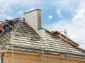 Deux couvreurs travaillent sur une toiture en cours de renovation. Des échafaudages entourent la maison.