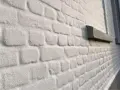 Mur en briques blanchies au badigeon à la chaux, avec un rebord de fenêtre en pierre sombre.