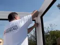 Pose d'un joint pour l'étanchéité véranda mur. Un ouvrier ajuste la structure blanche sous un ciel bleu.