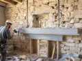 Un ouvrier ajuste une cheminée en béton devant une ouverture dans un mur en pierre.