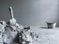 Une truelle repose sur un tas de ciment frais, prêt pour une utilisation ciment prompt sans sable. Un seau est visible au loin.