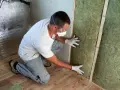 Un ouvrier installe de la laine de verre inflammable dans un mur, portant masque et lunettes de protection.