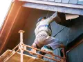 Un ouvrier sur échafaudage réalise l'isolation extérieure d'une maison. Une entreprise RGE pour des travaux d'isolation extérieure performants.