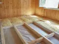 Isolation entre solives de plancher en cours. Laine de verre jaune posée dans la structure en bois.