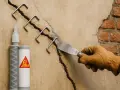 Réparation d'une micro fissure sur un mur de maison avec des agrafes métalliques et un produit Sika.