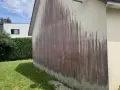 Traces sombres sur un mur extérieur, probablement dues à des algues rouges et à l'eau de javel.