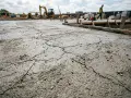 Dalle de béton fraîchement coulée présentant des fissures. Chantier en arrière-plan.