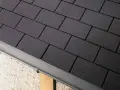 Détail d'une toiture en pose de bardeau bitumé gris foncé, avec une gouttière grise.
