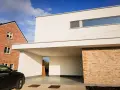 Maison moderne avec façade en crépi blanc immaculé, prête pour un nettoyage. Une voiture noire est garée sous l'auvent.