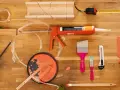 Pistolet à mastic acrylique, rouleau, pinceaux, ruban adhésif, mètre et boîte à onglets pour une utilisation en bricolage.