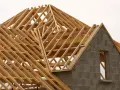 Structure en bois d'une charpente simple, en cours de construction. Les poutres de bois forment un motif complexe au-dessus des murs en blocs de béton.