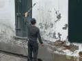 Un homme utilise un nettoyeur haute pression pour le sablage facade, révélant la brique sous l'enduit décrépit.