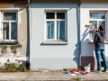 Un homme rénove une façade, appliquant un nouvel enduit soubassement. Des échantillons de couleurs et un pot de peinture sont prêts.