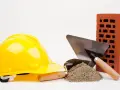 Casque jaune, brique rouge, tas de sable et truelles : les outils maçon essentiels pour bâtir.