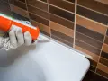 Application d'un joint acrylique ou silicone blanc pour étanchéifier le bord d'une baignoire contre un mur carrelé.