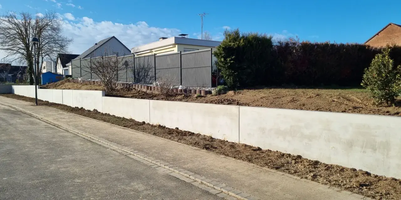 La **fondation mur de soutènement** en béton est prête pour le jardinage. Le ciel bleu et les maisons en arrière-plan annoncent le printemps.