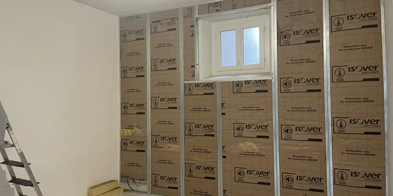 Pose de laine de verre ISOVER en 2 couches sur une structure métallique, avec une fenêtre au centre.