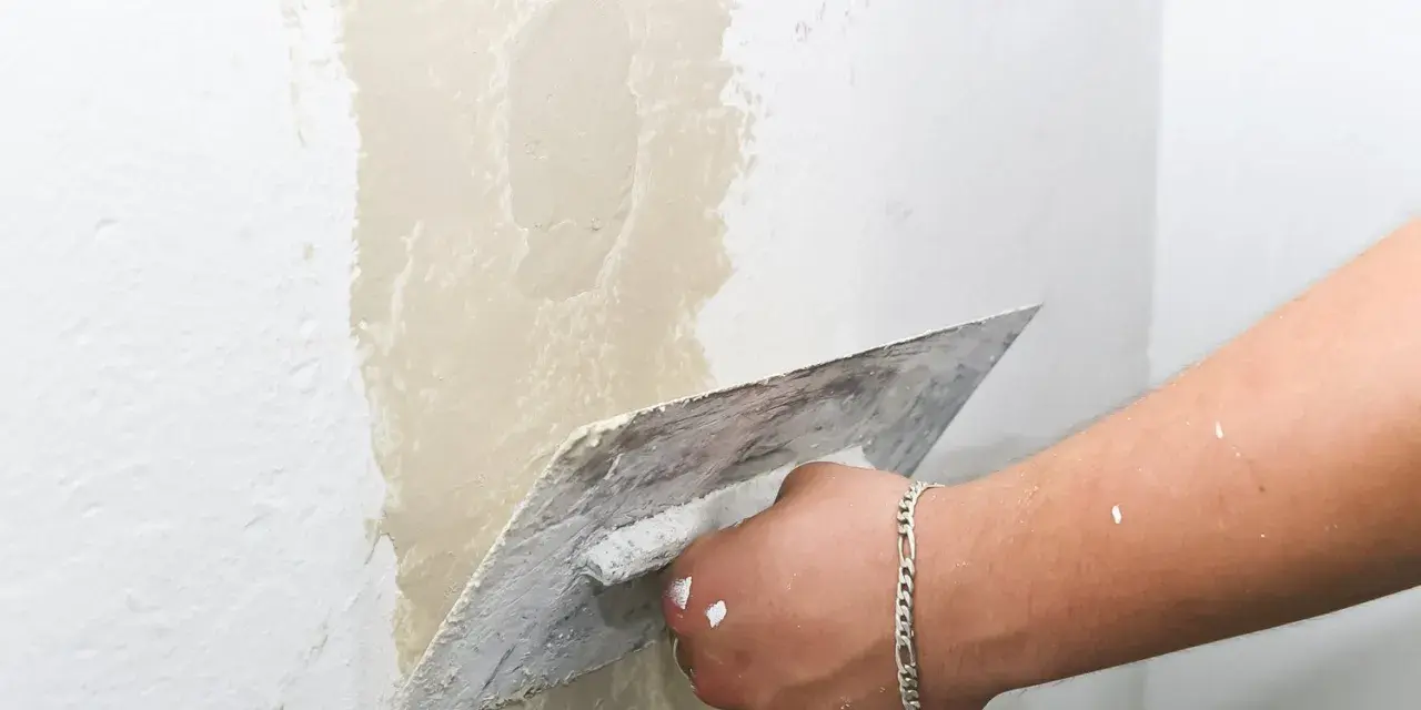 Main d'un artisan appliquant de l'enduit pour réparer une fissure crepis maison.