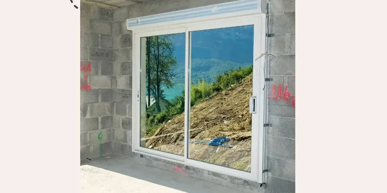 Fenêtre coulissante en PVC installée dans un mur en parpaings, offrant une vue sur un paysage montagneux. Idéal pour apprendre comment poser une fenêtre de toit.