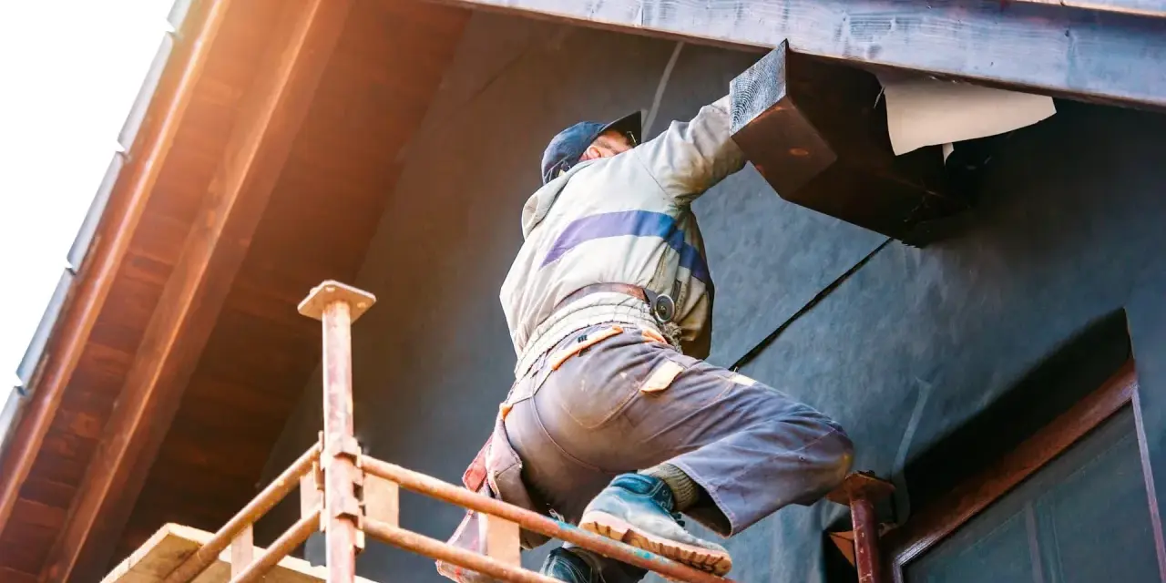Un ouvrier sur échafaudage réalise l'isolation extérieure d'une maison. Une entreprise RGE pour des travaux d'isolation extérieure performants.