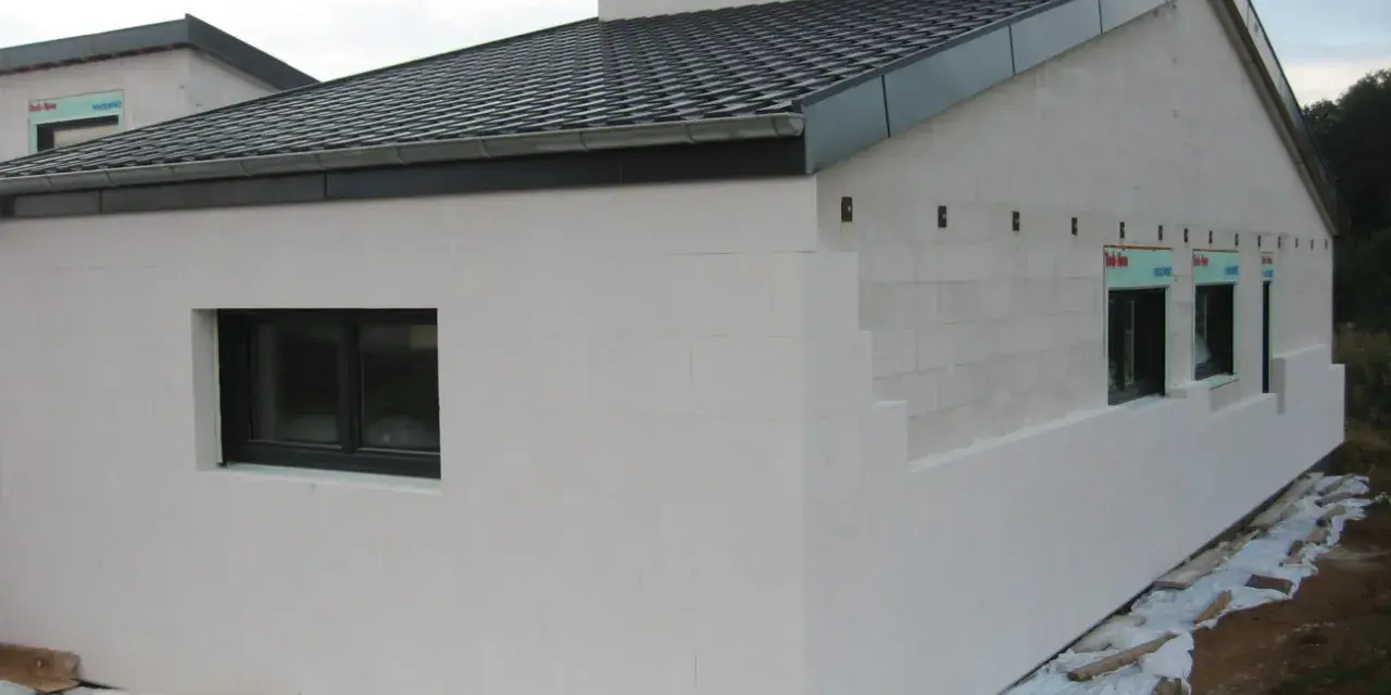 Maison en construction avec murs en **béton cellulaire extérieur**. Fenêtres noires et toit sombre.