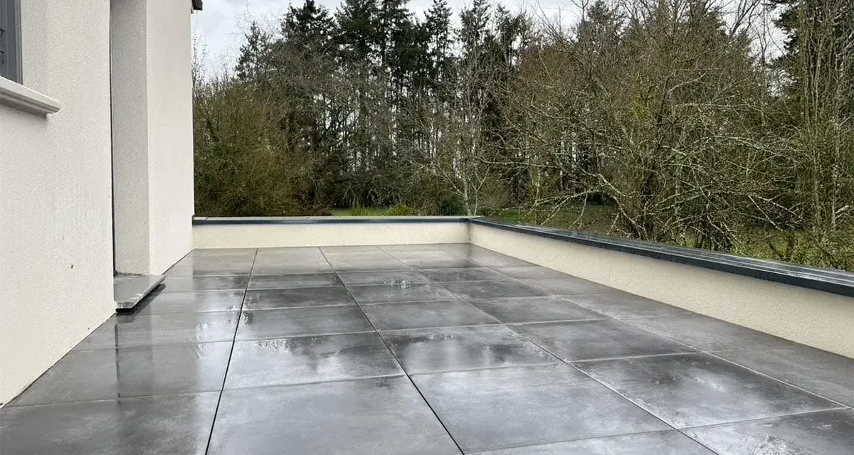 Terrasse avec dalles grises sur un toit plat, offrant une vue sur une forêt. L'étanchéité du toit plat est assurée pour une durabilité optimale.