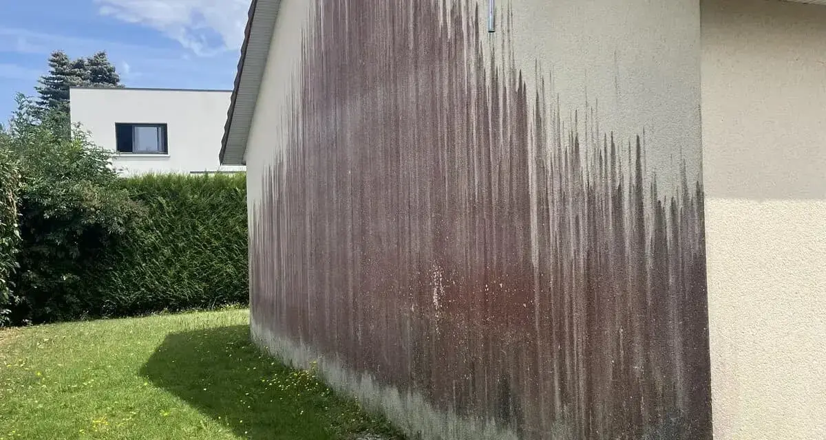 Traces sombres sur un mur extérieur, probablement dues à des algues rouges et à l'eau de javel.