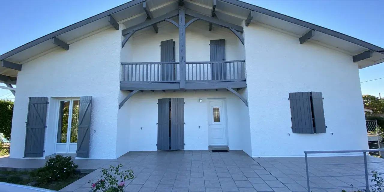 La façade maison 2 couleurs, blanche et grise, présente un balcon avec des volets assortis.