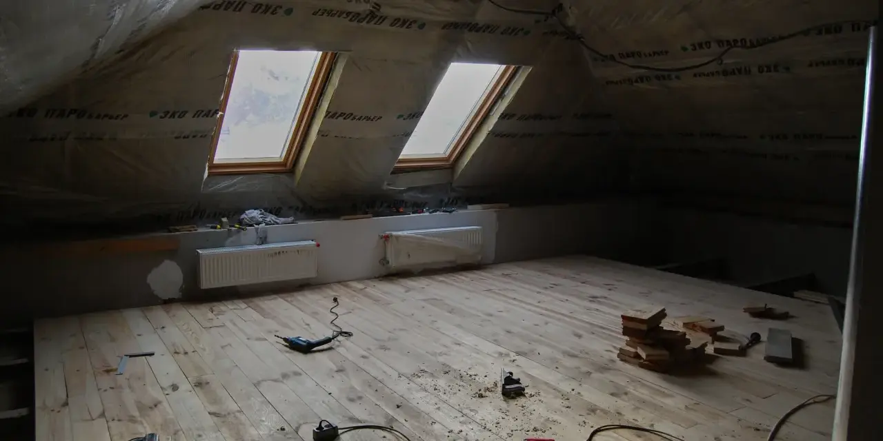 Grenier en cours d'aménagement, avec pare-vapeur fibre de bois, deux fenêtres de toit et un plancher en bois brut. Outils de bricolage au sol.