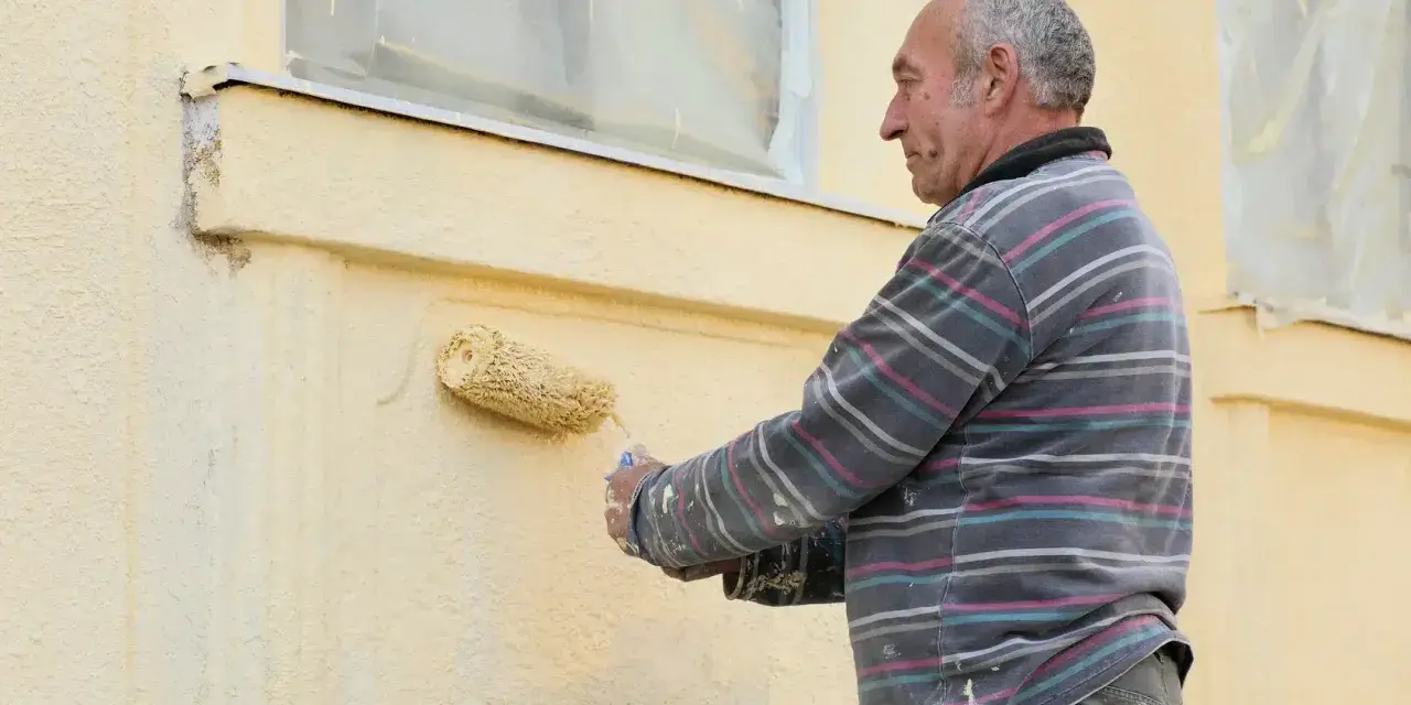Un homme peint une façade jaune avec un rouleau.
