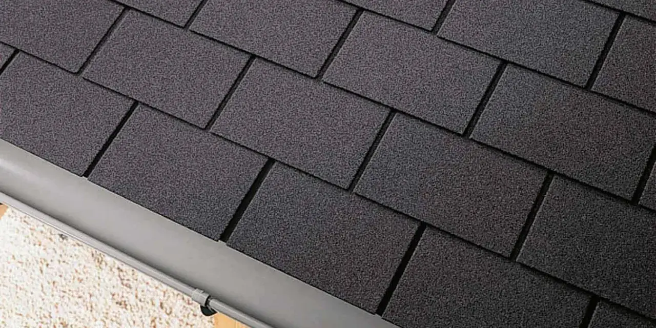 Détail d'une toiture en pose de bardeau bitumé gris foncé, avec une gouttière grise.