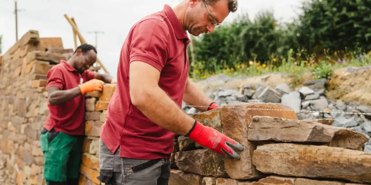 Deux maçons construisent un mur en pierre sèche.
