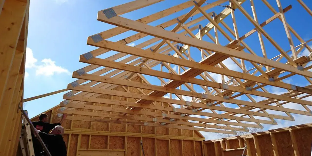 Construction d'une charpente fermette en bois sous un ciel bleu. Des ouvriers travaillent sur l'installation.