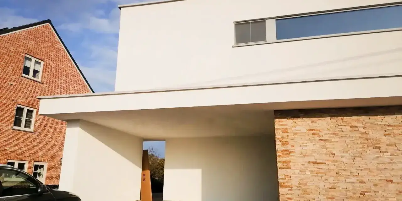 Maison moderne avec façade en crépi blanc immaculé, prête pour un nettoyage. Une voiture noire est garée sous l'auvent.
