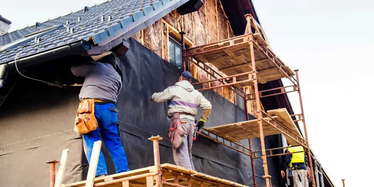 Travailleurs sur échafaudages installent une membrane pour l'isolation par l'extérieur d'une maison en construction.