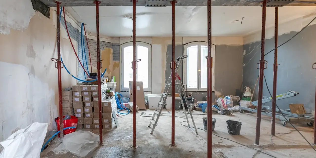 Chantiers : étais métalliques soutenant une poutre en cours de consolidation pour le prix d'une fondation maison. Matériaux et outils de construction visibles.