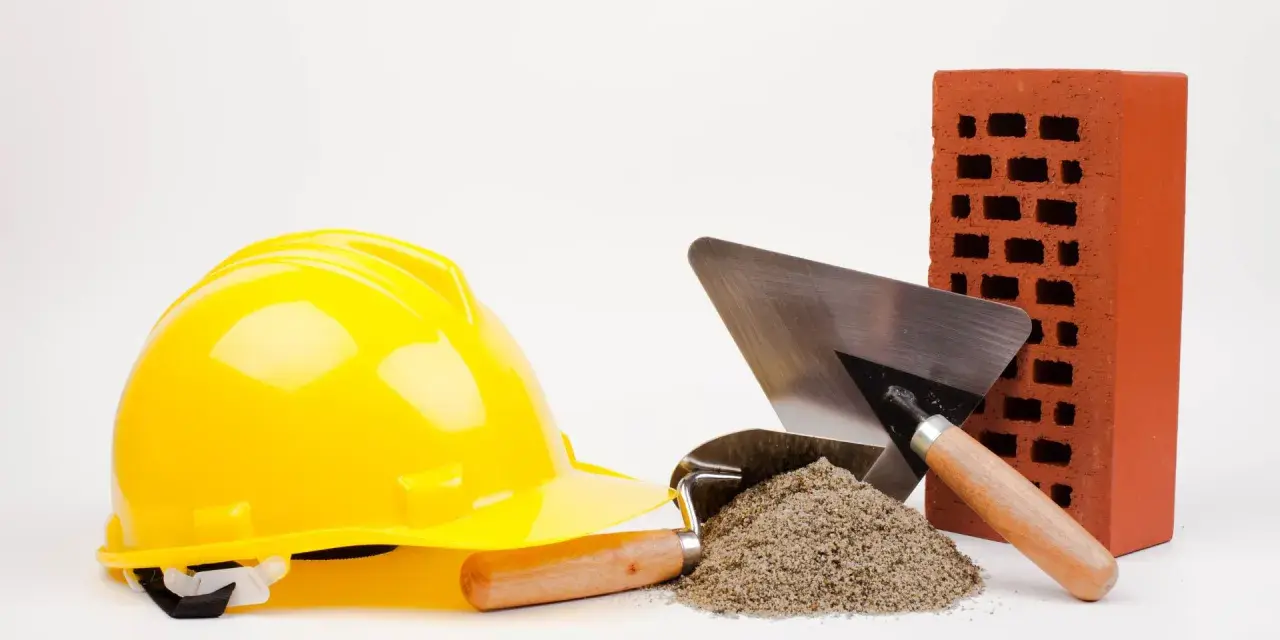 Casque jaune, brique rouge, tas de sable et truelles : les outils maçon essentiels pour bâtir.