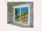 Fenêtre coulissante en PVC installée dans un mur en parpaings, offrant une vue sur un paysage montagneux. Idéal pour apprendre comment poser une fenêtre de toit.
