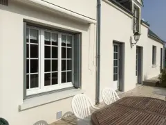 Un grand **appui de fenêtre** blanc orne la façade d'une maison. Des volets gris sont partiellement ouverts.