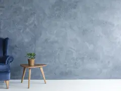 Fauteuil bleu profond devant un mur texturé avec une peinture effet stucco. Une petite table en bois supporte une plante verte.