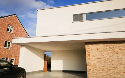 Maison moderne avec façade en crépi blanc immaculé, prête pour un nettoyage. Une voiture noire est garée sous l'auvent.