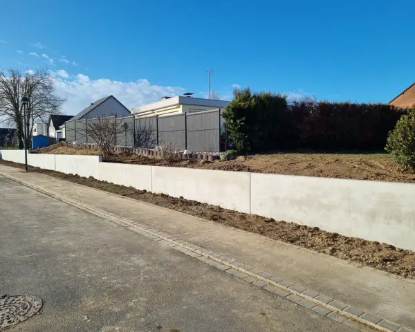 La **fondation mur de soutènement** en béton est prête pour le jardinage. Le ciel bleu et les maisons en arrière-plan annoncent le printemps.