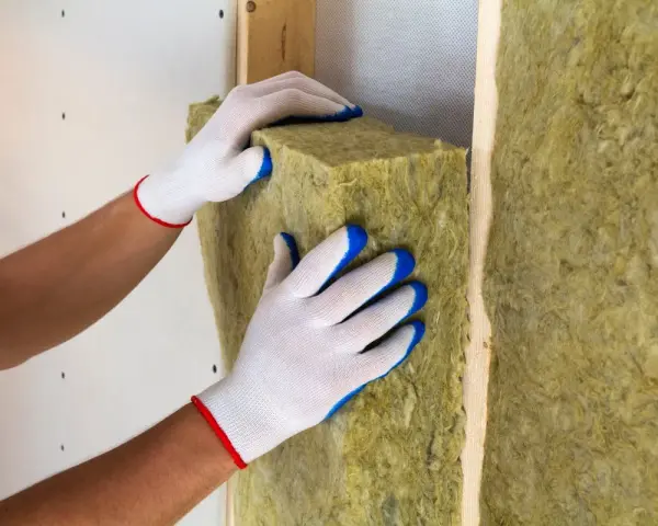 Pose d'isolant en laine de roche dans un mur. Les mains gantées ajustent le matériau pour une isolation optimale.